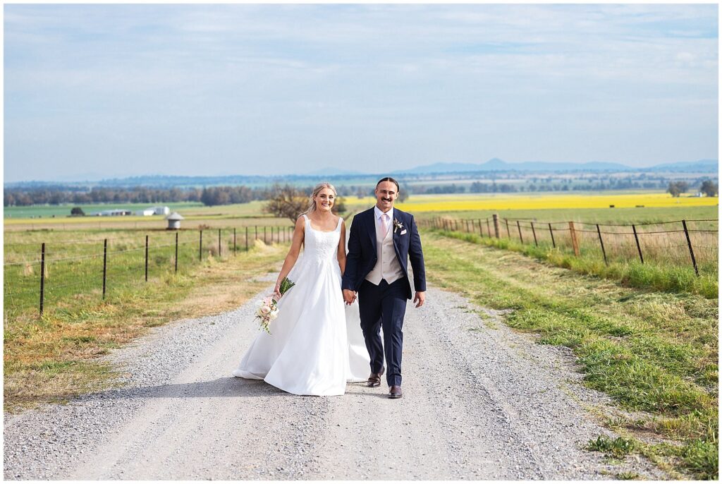 walking on a country road near Attunga nsw a couple in a wedding dress and suit holds hands and smile and laugh