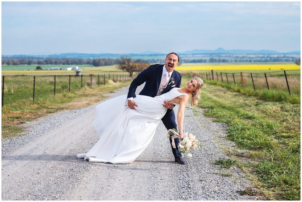 walking on a country road near Attunga nsw a couple dip each other as the groom laughs huge their is a canola crop in the background
