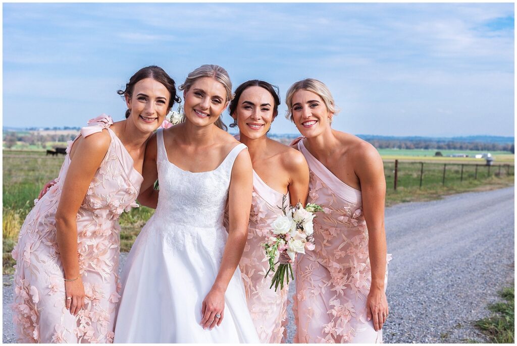 a bride and her bridesmaid in dusty pink dresses hug each other in the country side near ATtunga NSW