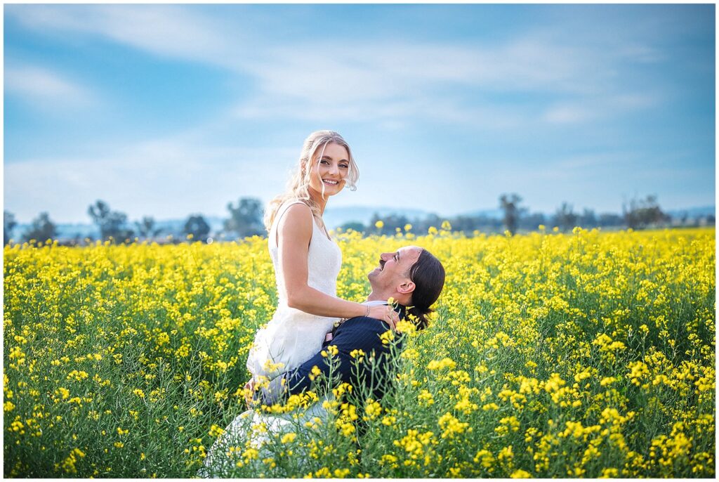 a groom lifts his bride in the canola fields as she smiles near Manilla NSW