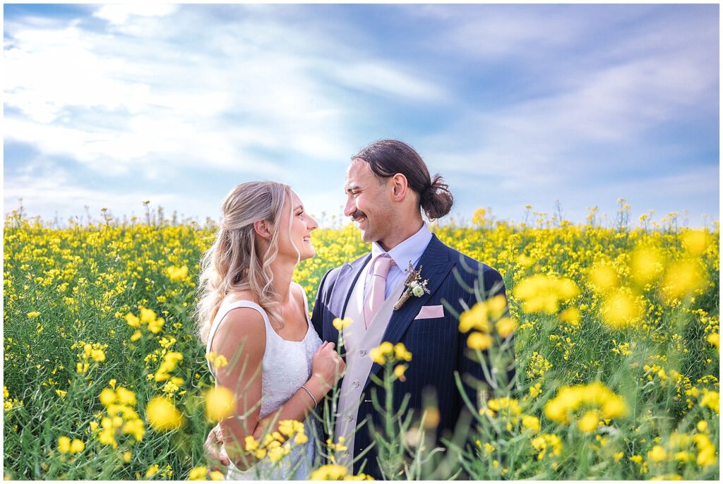 a bride and groom look into each others eyes amongst a yellow canola crop Near Tamworth NSW the sky is blue