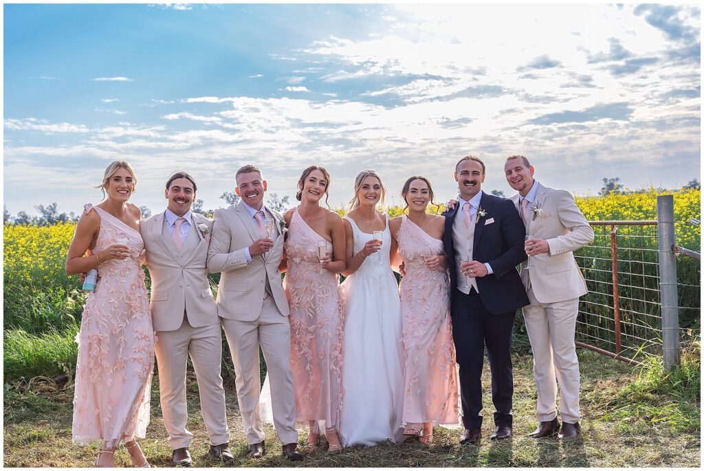 a bridal party share a drink together amongst a yellow canola crop on a farm near Tamworth NSW