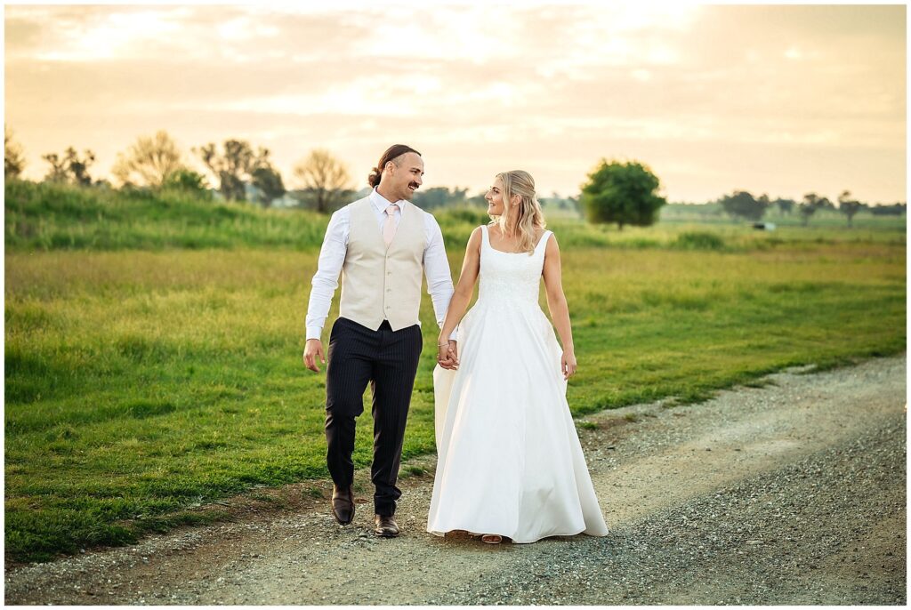 walking in the long golden grass for a bride and grooms holding hands as her dress drags as the sunsets over Tangarratta