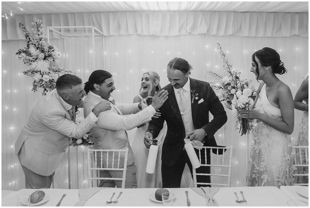 a bride and two groomsmen laugh huge at a groom who is holding smoke bombs in his arms